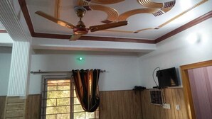 Una habitación con techo de madera, ventilador de techo, ventana con cortinas y televisor montado en la pared.
