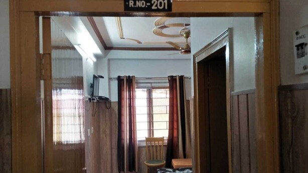 Una habitación con cama, una silla, un escritorio y un ventanal con cortinas.