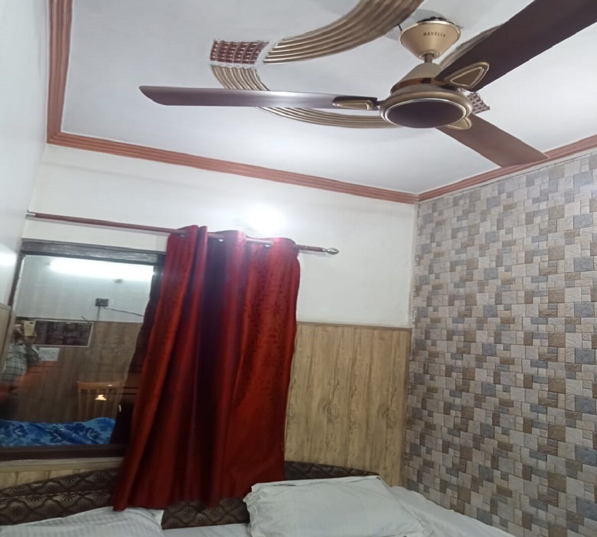 A bedroom with a bed, a red curtain, a ceiling fan, and a tiled wall.