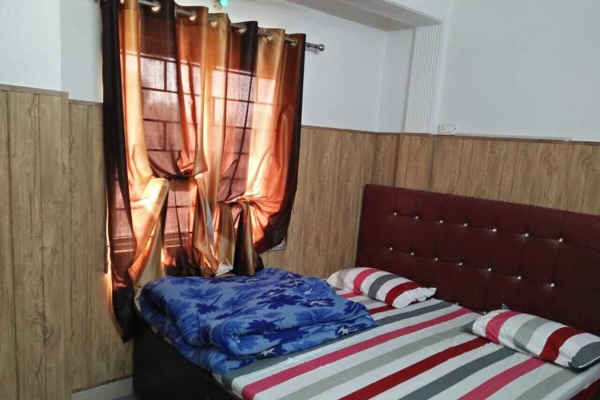 A bedroom with a wooden headboard, a bed with striped bedding, and curtains.