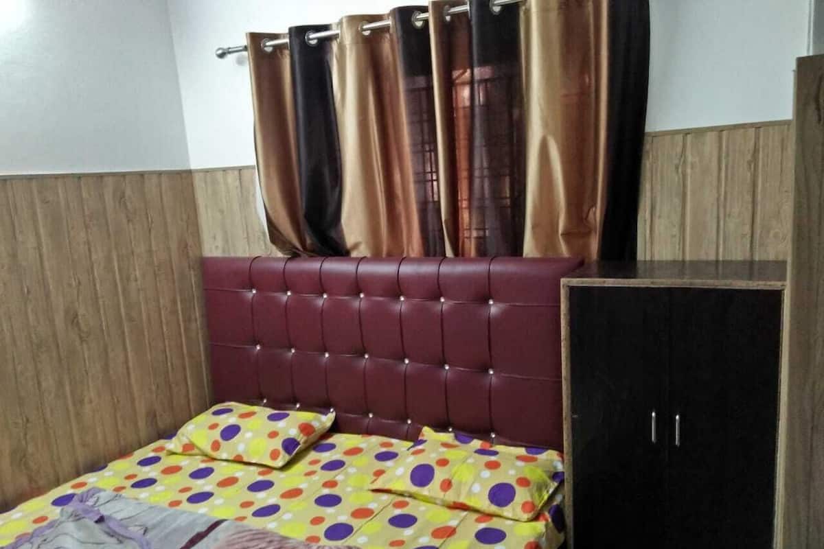 A bedroom with a tufted headboard, a bed with polka dot bedding, a wooden wardrobe, and curtains.
