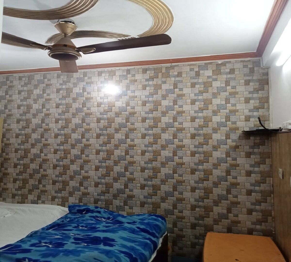 A bedroom with a bed, a small table, a ceiling fan, and a tiled wall.