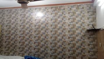 A bedroom with a bed, a small table, a ceiling fan, and a tiled wall.