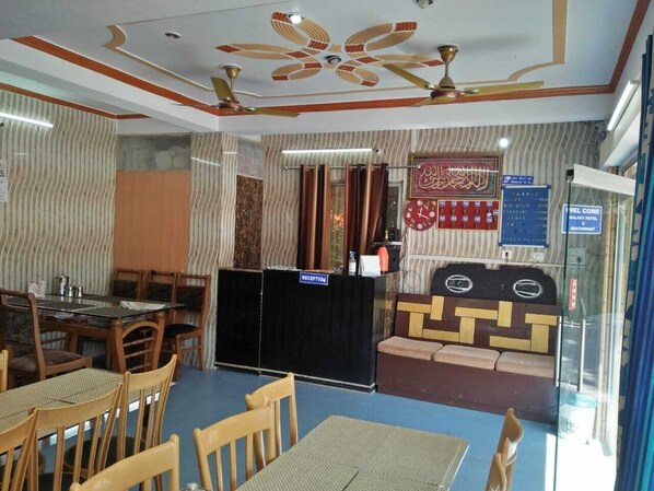 A reception area with a reception desk, a seating area with sofas, and a dining area with tables and chairs. - Galaxy Hotel (Lansdowne)