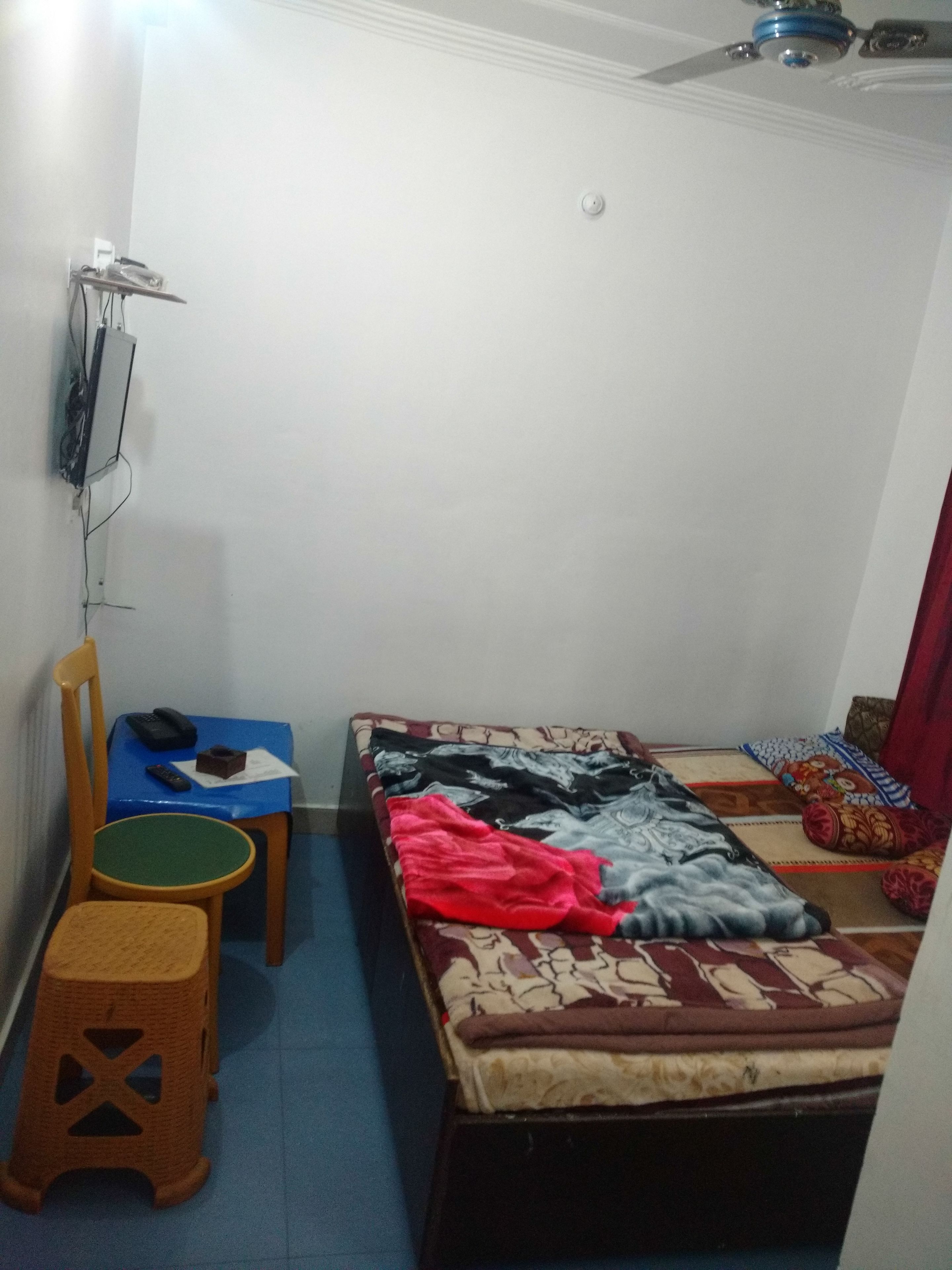 Una habitación pequeña y poco amueblada con una cama individual, una silla, una mesita y un calentador en la pared.