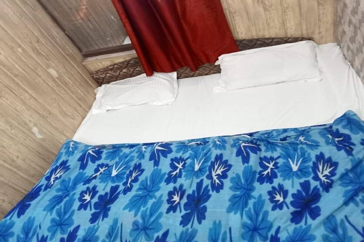 A bed with a blue floral bedspread, white pillows, and a red curtain.