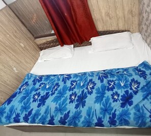 A bed with a blue floral bedspread, white pillows, and a red curtain. - Galaxy Hotel (Lansdowne)
