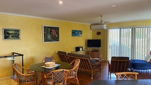 Una sala de estar con comedor, que incluye muebles de mimbre, un televisor de pantalla plana y obras de arte en las paredes.