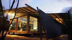 A modern house with a glass facade, a wooden deck, and a metal roof structure.