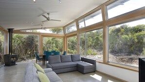 A modern interior with a sectional sofa, a dining area, and large windows offering a view of the outdoors.