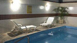 Una piscina interior con sillas reclinables blancas y una planta en maceta.
