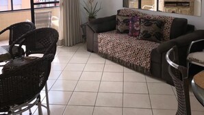 Una sala de estar con sofá, sillas, televisor y un balcón con vistas a edificios.