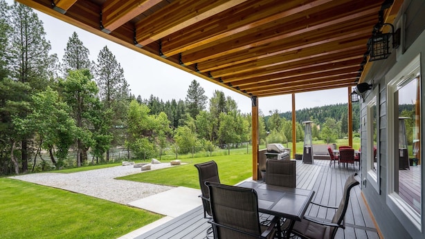Une terrasse extérieure couverte, dotée d’une plateforme en bois, d’une table avec des chaises et offrant une vue sur un jardin aménagé et une forêt.