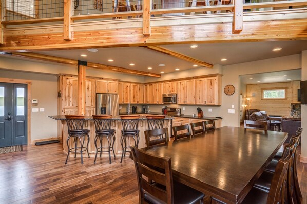 A spacious kitchen with wooden cabinets, a large island with stools, and a dining area with a long table and chairs.