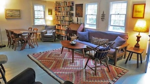 A cozy living room with a sofa, armchairs, a coffee table, a bookshelf, and a dining area with chairs and a table.