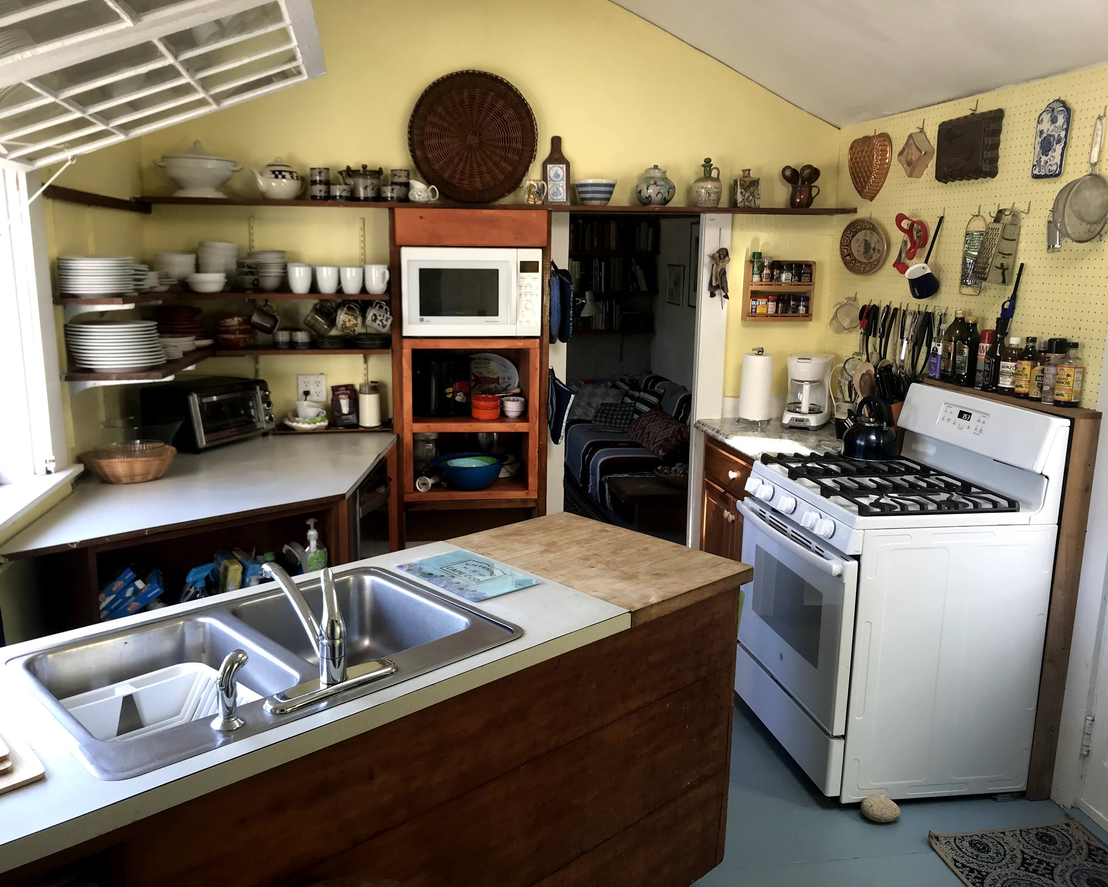 A compact kitchen with a microwave, stove, and sink. There are shelves with dishes and a coffee maker.