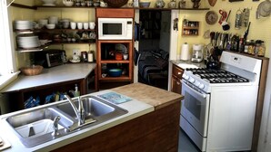 A compact kitchen with a microwave, stove, and sink. There are shelves with dishes and a coffee maker.