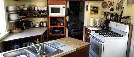 A compact kitchen with a microwave, stove, and sink. There are shelves with dishes and a coffee maker.