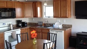 A kitchen with wooden cabinets, a dining table with chairs, a ceiling fan, and a television mounted on the wall.