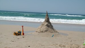 Une plage de sable avec un château de sable, une pelle et une petite excavatrice jouet.