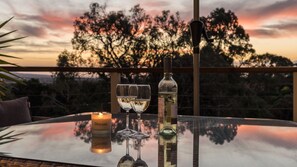 A table with a candle, two wine glasses, and a bottle of wine on a balcony with a sunset view. - Mount Eliza Sunset Apartment (Mount Eliza)