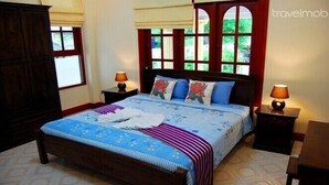 A neatly made bed with a blue and white floral bedspread, two nightstands with lamps, and a large window with a view of greenery.