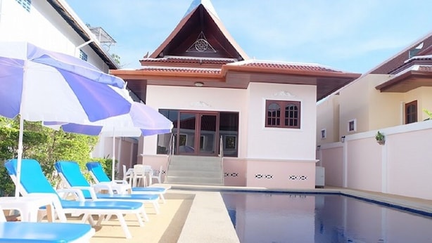 A swimming pool area with lounge chairs and umbrellas, a building with a sloped roof, and a clear sky.