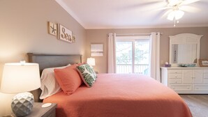 A bedroom with a bed, nightstand, lamp, decorative wall art, ceiling fan, and a window with curtains.
