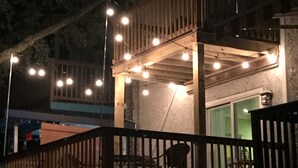 A multi-level wooden deck with string lights, a balcony, and a view of a building with a green door.