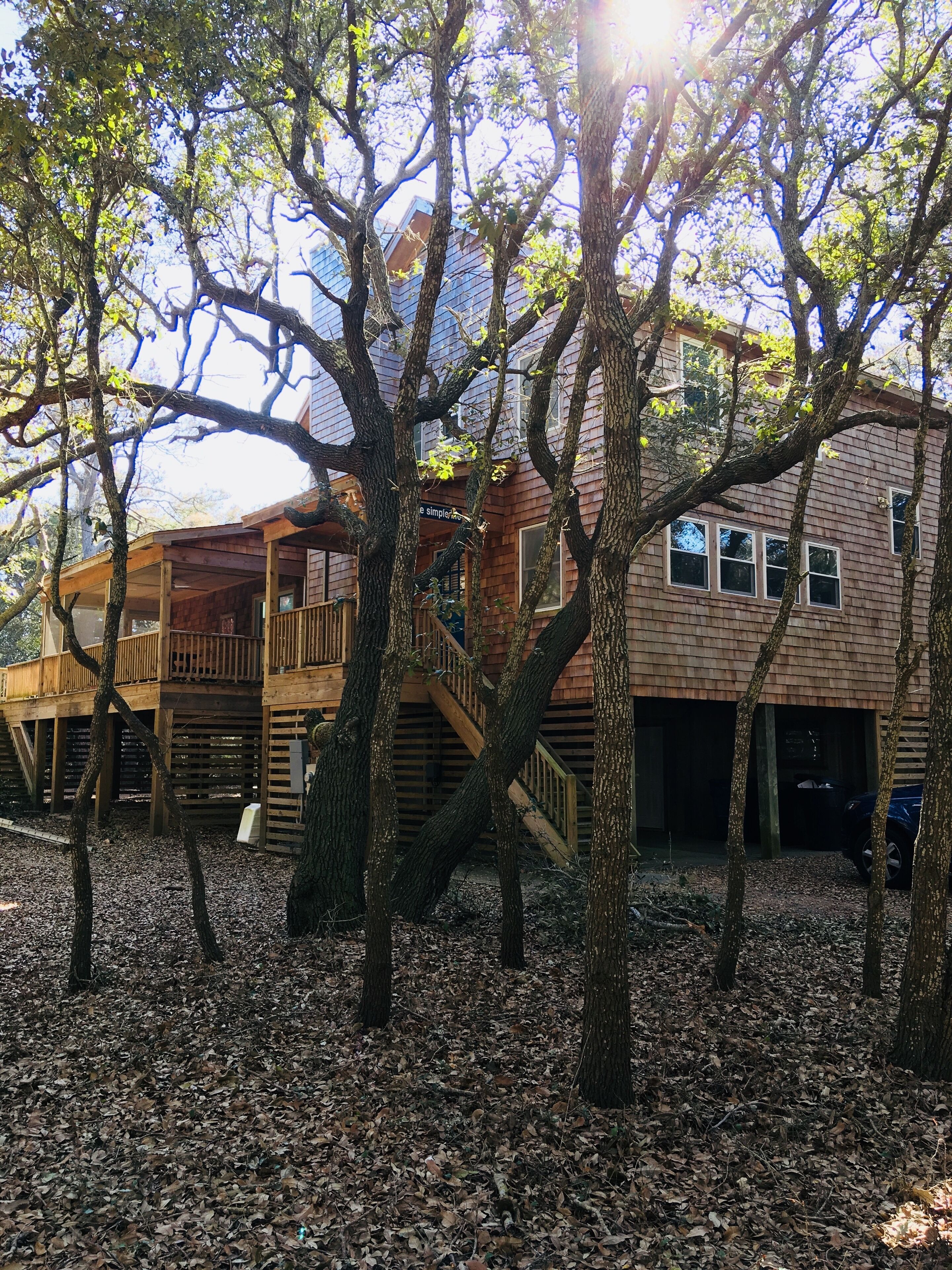 A wooden house with a deck and stairs, surrounded by trees and leaves.