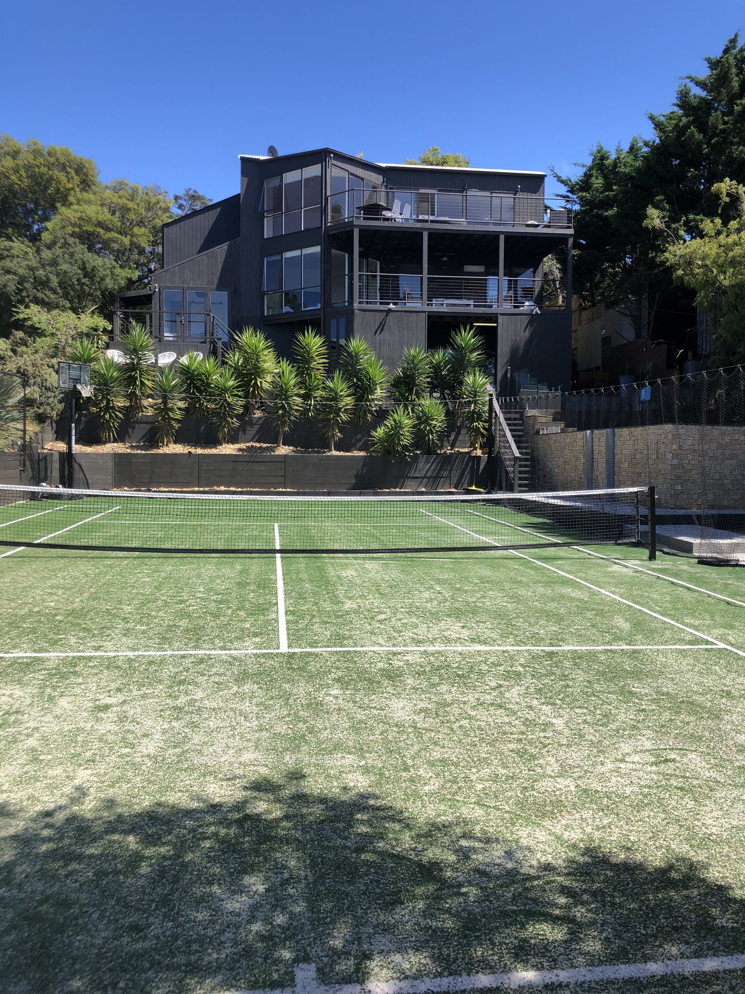 Una cancha de tenis con una red, rodeada por un edificio de varios pisos y balcones.