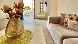 Una sala moderna con un sofá, una mesa de centro con un jarrón de flores secas, una lámpara colgante original y vistas al exterior a través de una puerta abierta.