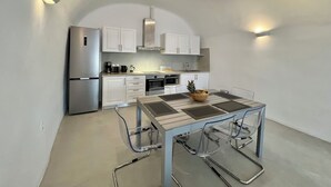 Una cocina moderna con armarios blancos, electrodomésticos de acero inoxidable y una mesa con cubierta de vidrio transparente.