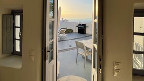 Una puerta abierta que da a un balcón con una parrilla y una mesa, con vistas a un paisaje pintoresco.