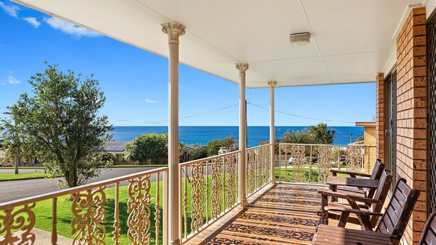 A covered balcony with a view of the ocean, featuring a patterned floor and wooden furniture. - Grandview House - Ocean Views (KIANGA)