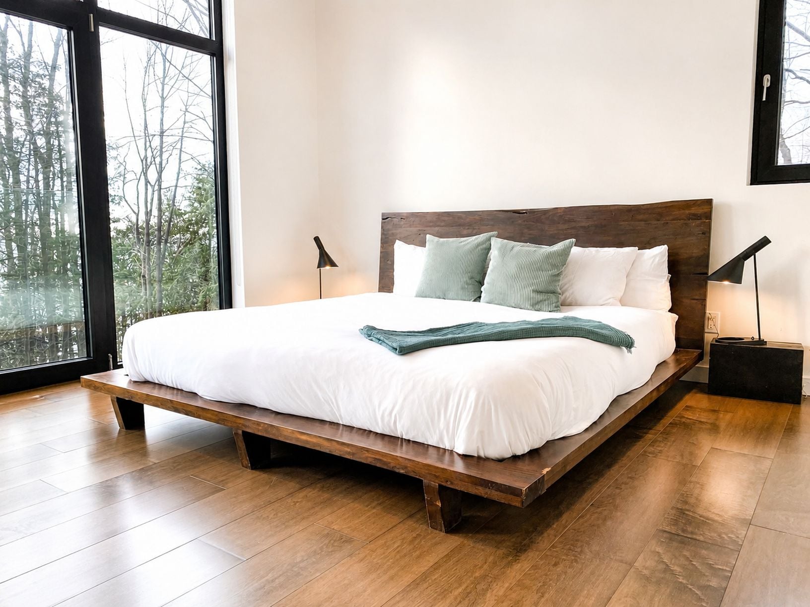 A modern bedroom with a large bed, wooden headboard, and a view of trees through the window.