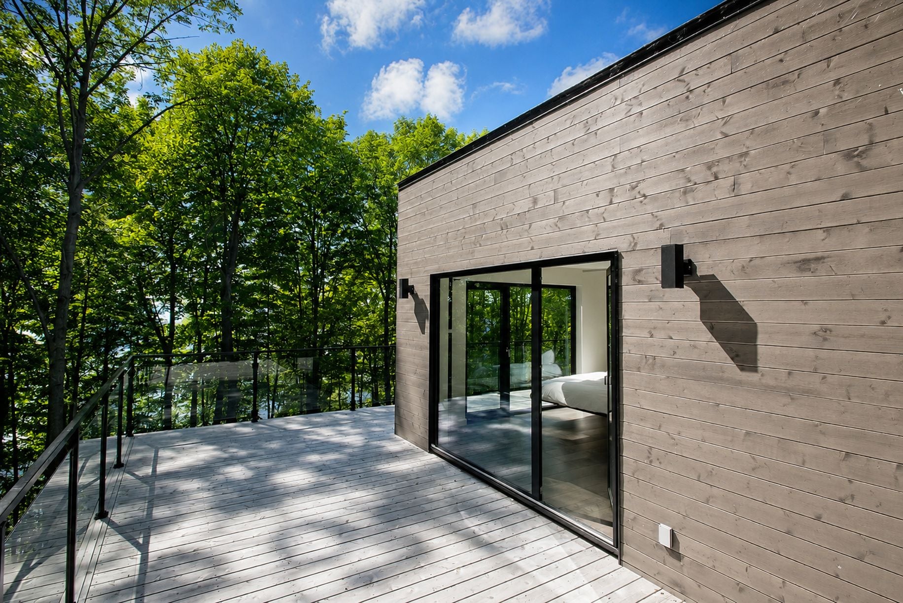 Un bâtiment moderne avec une façade en bois, de grandes portes vitrées et une terrasse dotée d’une rambarde.