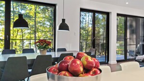 A modern dining area with a large table, chairs, and a bowl of apples. - Cozy lakefront Retreat with Spa Pet Friendly (St-Armand)