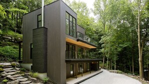 A modern two-story house with a balcony, surrounded by a forested area. - Cozy lakefront Retreat with Spa Pet Friendly (St-Armand)