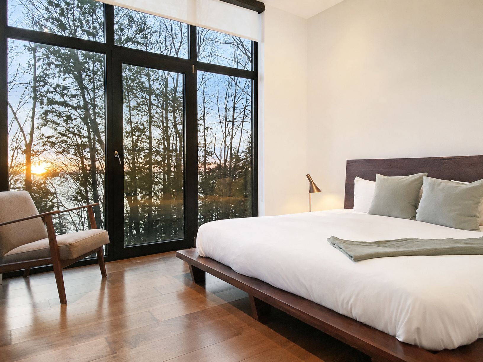 Ein Schlafzimmer mit großem Fenster, einem Bett, einem Sessel und einem Nachttisch.