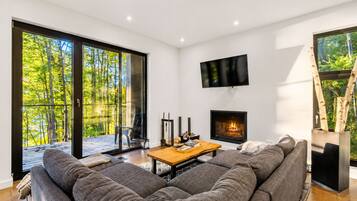 A modern living room with a large sofa, a fireplace, a television, and a sliding glass door leading to a deck.