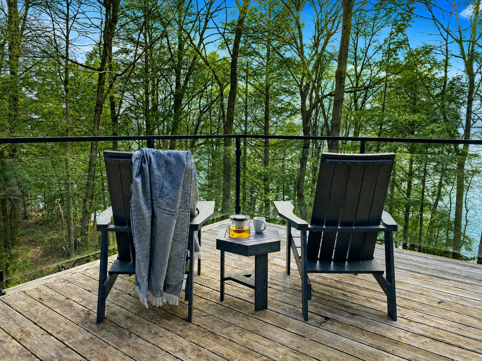 Zwei Stühle auf einer Holzterrasse mit Blick auf einen Wald und ein Gewässer.
