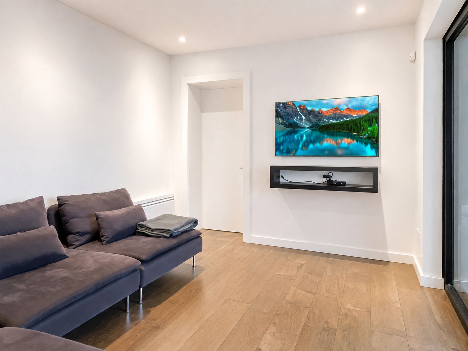 Un salon moderne avec un canapé gris, un téléviseur fixé au mur et un plancher en bois.