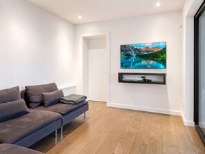 A modern living room with a grey sofa, a mounted TV, and a wooden floor. - Lakefront Private Oasis Hot Tub Pet Friendly (St-Armand)