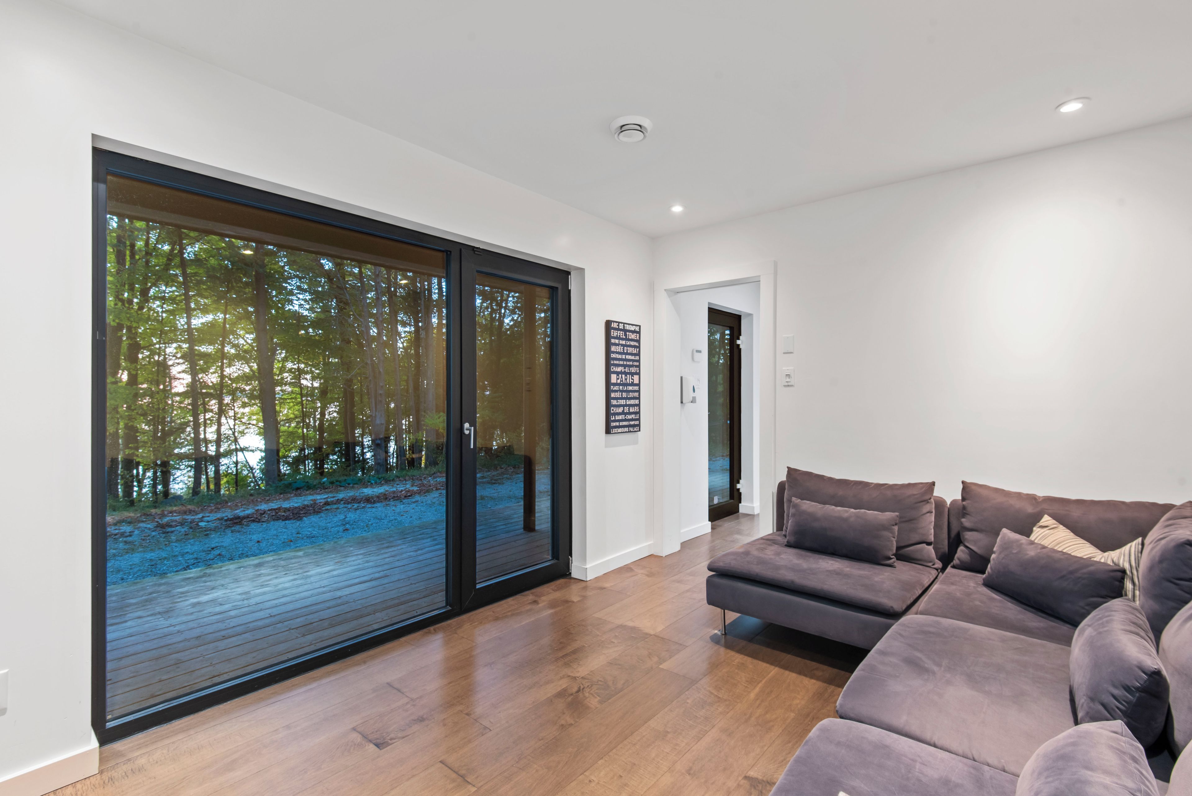 A modern living room with a large sliding glass door leading to a forest view, a sectional sofa, and a minimalist design.