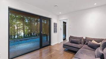 A modern living room with a large sliding glass door leading to a forest view, a sectional sofa, and a minimalist design.
