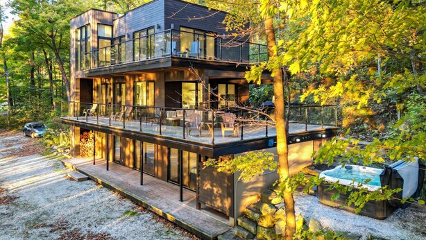 A modern two-story house with a glass balcony, surrounded by trees. - Cozy lakefront Retreat with Spa Pet Friendly (St-Armand)