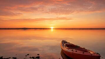A calm body of water with a sunset, a rowboat, and a rocky shoreline.