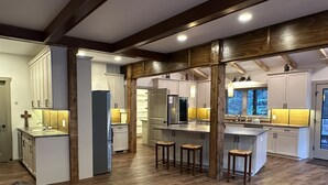 A spacious kitchen with wooden beams, white cabinets, and a central island with stools. - Hosting a retreat, family reunion, girls or couples weekend or special occasion? (Ellijay)