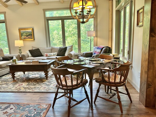 A cozy living room with a dining table, wooden chairs, a sofa, and a chandelier. - Hosting a retreat, family reunion, girls or couples weekend or special occasion? (Ellijay)